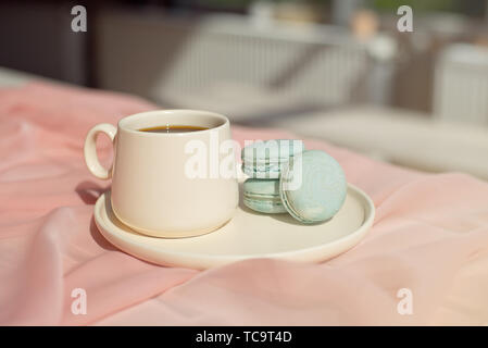 Francese amaretto blu e la tazza di caffè in piedi su un tavolo di legno con una tovaglia rosa bianco Vaso con fiori rosa e verde. Foto Stock