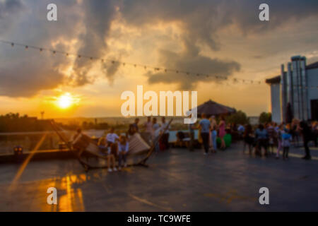 Defocalizzata persone che frequentano open air summer party sul tetto. Caldo sole di luce nella sera. Foto Stock