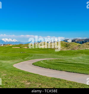 Telaio quadrato vasto campo erboso con curvatura strada lastricata e case al di là delle piste Foto Stock