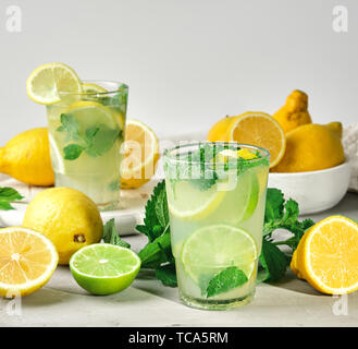 Bevanda rinfrescante limonata con limoni, foglie di menta, lime in un bicchiere , accanto a gli ingredienti per la realizzazione di un cocktail Foto Stock