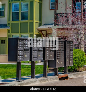 Telaio quadrato di cassette postali cluster sul marciapiede davanti alle case visto in una giornata di sole Foto Stock