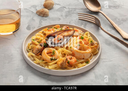 Piatti di pasta. Tagliolini con cozze, gamberi, vongole e anelli di totano con un bicchiere di vino bianco Foto Stock