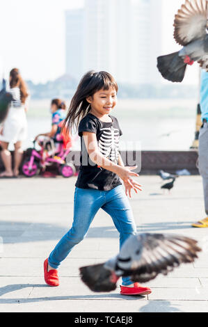 Una giovane ragazza cambogiana cagna i piccioni lungo la passeggiata di fronte al Palazzo reale a Phnom Penh, Cambogia. Foto Stock