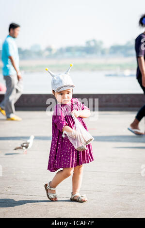 Una bambina carina si nutre felicemente dei piccioni lungo il lungomare di Phnom Penh, Cambogia. Foto Stock