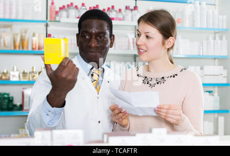 Americano africano farmacista maschio spiegando la medicina prescritta alla giovane donna in farmacia Foto Stock