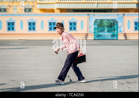 Una vecchia signora cambogiana fa il suo modo attraverso la strada di fronte al Grand Palace, Phnom Penh Cambogia del Sud Est Asiatico. Foto Stock