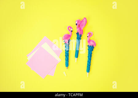 Flatlay Desktop: penna con flamingo e carta rosa giacente vivace sfondo giallo Foto Stock