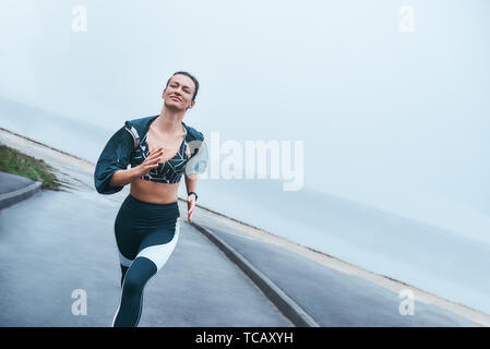 La mia motivazione quotidiana. Felice e forte donna disabile in abbigliamento sportivo è in esecuzione all'aperto vicino al mare e sorridente. Sport concept. Sportivo disabili Foto Stock