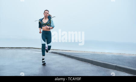 Vi sono più forti di quanto si pensi. Incredibile forte donna disabile in abbigliamento sportivo è in esecuzione all'aperto vicino al mare. La motivazione. Sport concept. Sportivo disabili Foto Stock