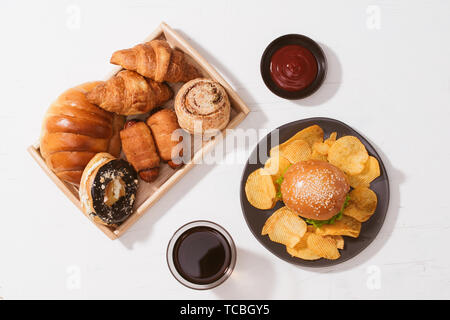 Pane appena sfornato, panini, grandi hamburger sul tavolo bianco - cibo malsano concetto Foto Stock