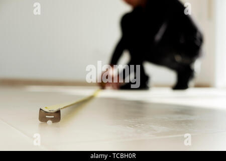 Primo piano di un giovane uomo caucasico utilizzando un nastro di misurazione su un beige pavimento piastrellato Foto Stock