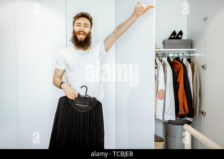 Ritratto di un divertente ed entusiastico uomo cercando femmina nero mantello in armadio a casa Foto Stock