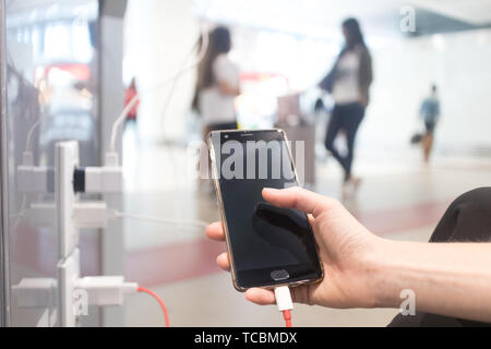 Mani femminili holding e utilizza lo smartphone durante la ricarica è in un luogo pubblico tramite spina elettrica e un cavo di ricarica Foto Stock