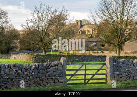 Il pittoresco villaggio di Downham, Lancashire, in serata sole, Ribble Valley, Regno Unito guardando verso la chiesetta di San Leonardo che si trovano di fronte un cancello in legno Foto Stock