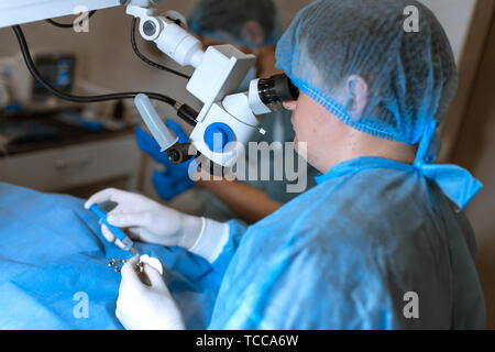 Oculista chirurgo guardando attraverso il microscopio chirurgico facendo operazione difficoltosa. Foto Stock