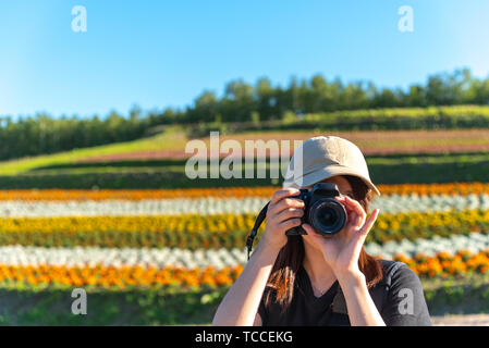 Close-up di una giovane ragazza giapponese in possesso di una fotocamera digitale e prendendo la foto in un colorato campo dei fiori in estate giornata soleggiata a Shikisai-no-oka Foto Stock