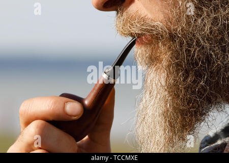 Uomo Barbuto tenendo un tubo di fumo nella sua bocca, vista laterale Foto Stock