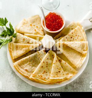 Tradizionale russo pancake con caviale rosso e il burro sul tavolo e due bicchieri di vodka Foto Stock