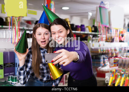 Comically vestito le fanciulle felici rendere divertente selfies foto nella festosa negozio di accessori Foto Stock