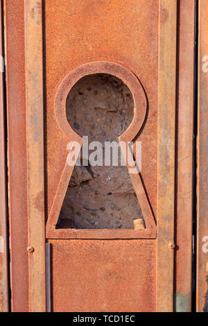 Keyhole di grandi dimensioni in un metallo arrugginito porta con una vista della parete di roccia alle spalle Foto Stock