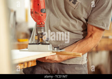 L uomo non identificabili indossando grigio Camicia manica corta e vite di perforazione nel rinforzo di metallo che è seduto sulla parte superiore dell'asse di legno Foto Stock