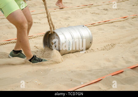Un uomo in pantaloncini corti tira una corda allacciate con fune sulla sabbia. Competizioni sportive. Foto Stock