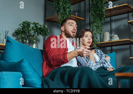 Basso angolo di vista sconvolto l uomo azienda controller remoto durante la visione di un filmato con la donna a casa Foto Stock