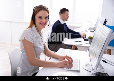 Ritratto di giovane imprenditrice sorridente utilizzando Computer seduti su una sedia che indossa la cuffia al lavoro Foto Stock