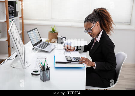 Felice giovane imprenditrice calcolo fattura sullo schermo del computer vicino al laptop Foto Stock