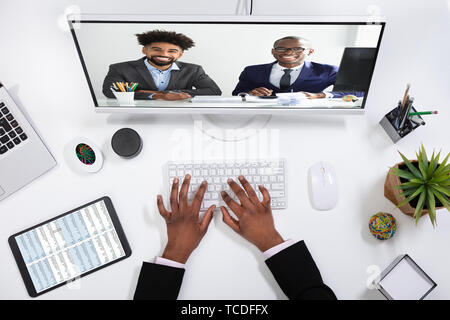 Vista laterale di una giovane imprenditrice la videoconferenza con i suoi colleghi sul computer Foto Stock