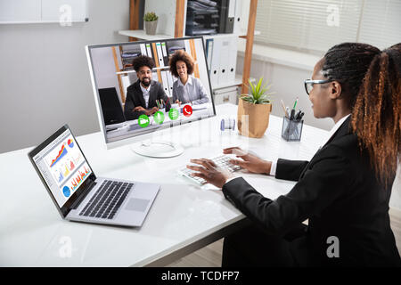 Sorridente giovane imprenditrice la videoconferenza con i suoi colleghi sul computer portatile vicino Foto Stock