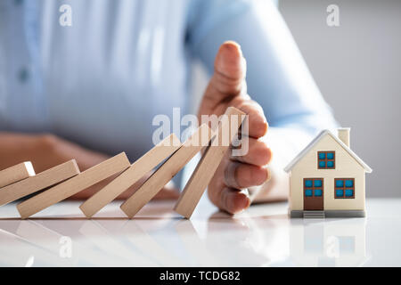 Close-up di un imprenditore la mano della casa di protezione modello dalla caduta dei blocchi di legno sulla scrivania Foto Stock