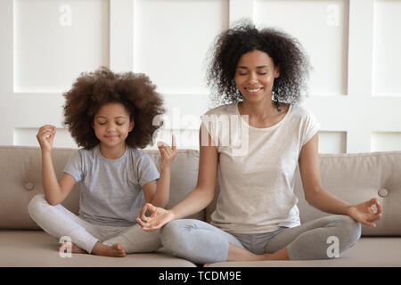 Sana madre africana Insegnare la meditazione seduti con la figlia sul divano Foto Stock