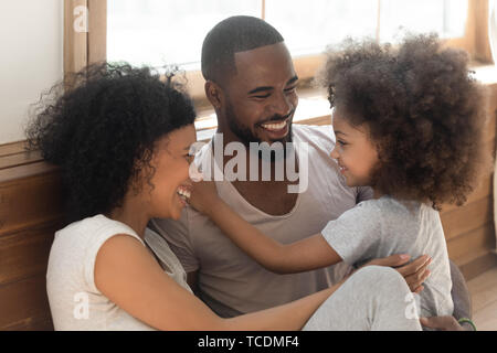 Nero felice famiglia bonding ridere sedersi sul pavimento della camera Foto Stock