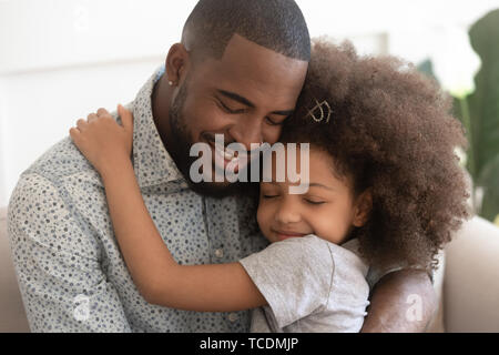 Amorevole padre africano abbraccio carino bambino figlia con gli occhi chiusi Foto Stock