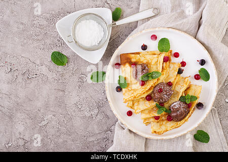 Frittelle con frutti di bosco e cioccolato decorato con foglie di menta. Una gustosa prima colazione. Vista superiore Foto Stock