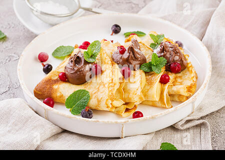 Frittelle con frutti di bosco e cioccolato decorato con foglie di menta. Una gustosa prima colazione. Foto Stock