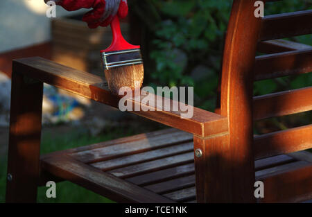 Mobili da giardino verniciatura a pennello. Pittura a mano la sedia in legno all'esterno. Foto Stock