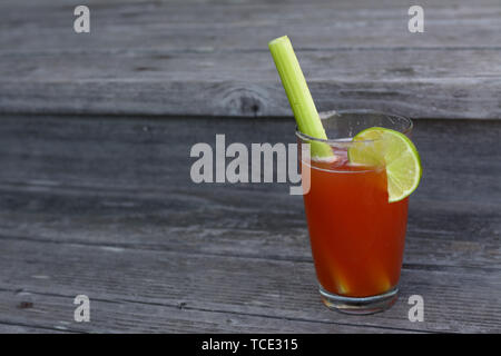 Una bevanda Clamato con sedano, sale e linea in una pinta bicchiere seduto su un vecchio ponte di legno. Foto Stock