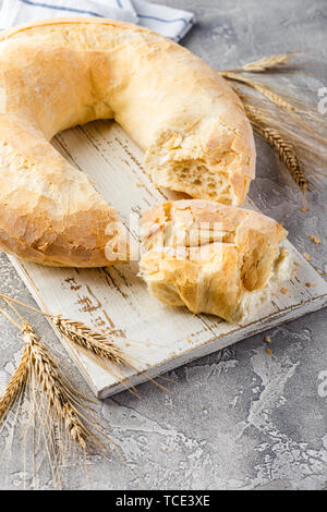 Grano pane rotondo nella forma di un anello e spikelets su un tagliere di legno su un calcestruzzo leggero sottofondo. Big bagel Foto Stock