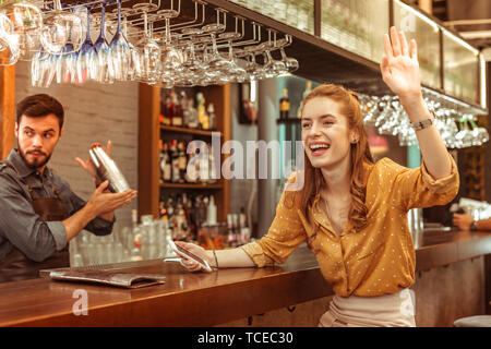 Sventolando la donna. Allegro gioiosa seducente affascinante bella i capelli rossi ridere bar visitatore emotivamente sventolare a qualcuno Foto Stock