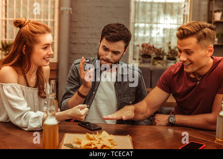 Per giocare con gli amici. Tre sorridenti allegro nice-appello giovani-adulti amici attraenti giochi al bar mentre avente le bevande Foto Stock