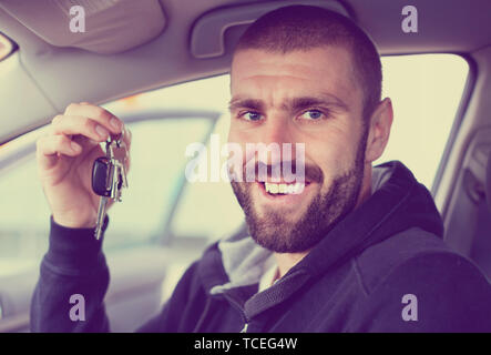 Giovane uomo con la barba contiene le chiavi per la sua nuova vettura nelle sue mani mentre è seduto in macchina Foto Stock