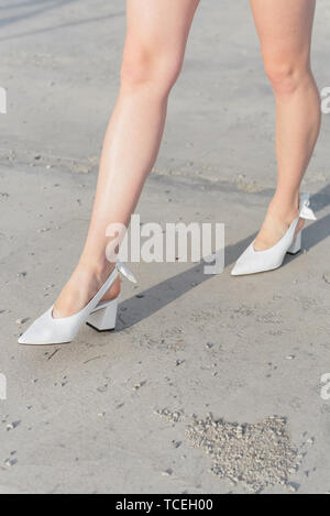 Scarpe bianche sulla ragazza in piedi. Le gambe nelle scarpe sono close-up. Una ragazza in scarpe alla moda passeggiate attraverso la citta'. Asfalto al calpestio Foto Stock