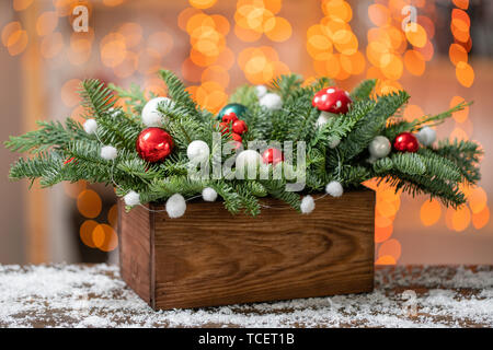 Bella disposizione festosa di abete rosso fresco con sfera di giocattoli in un rustico di una scatola di legno. Il Natale di umore. Bokeh ghirlanda di luci su sfondo. Foto Stock