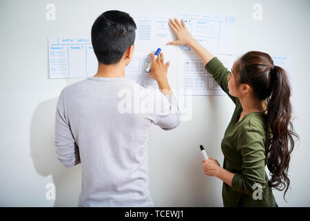 UX designer discutendo le immagini del sito web wireframe appeso alla parete office, vista dal retro Foto Stock
