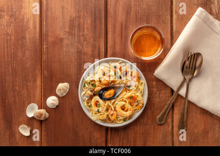 Piatti di pasta. Tagliolini con cozze, gamberi, vongole e anelli di totano, con un bicchiere di vino bianco, girato dalla parte superiore Foto Stock
