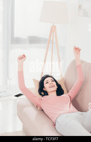 Bella Donna sorridente con le mani alzate in appoggio sul lettino a casa Foto Stock