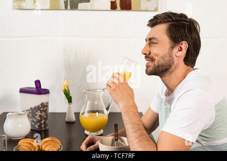 Sorridente uomo barbuto tenendo un bicchiere di succo di arancia durante la prima colazione Foto Stock