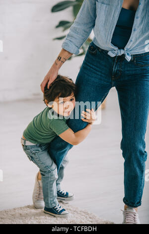 Carino il bambino in verde t-shirt abbracciando la mamma in salotto Foto Stock